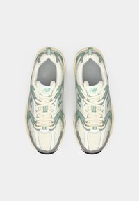 Pár fehér és világoszöld New Balance futócipő fűzővel, felülnézetből, síma fehér háttér előtt.