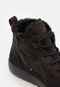 Brązowe skórzane buty typu mid-top z teksturowaną cholewką, czarnymi zamszowymi akcentami, futrzanym kołnierzem, bocznym zamkiem błyskawicznym i czarnymi sznurowadłami zapewniającymi pewne dopasowanie.