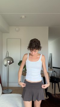 Valge ribadega tops ja tumedashall laienev mini seelik. Seeliku peal on elastne vöökoht. Kaasaegne siseruum, kus on minimalistlik sisustus.