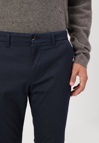 Marineblaue Hose aus strukturiertem Stoff, mit Knopfverschluss, Gürtelschlaufen und schrägen Seitentaschen. Die Passform ist maßgeschneidert und schmal.
