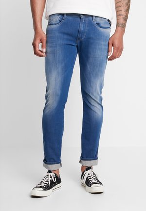 Jean en denim bleu à coupe slim, texture délavée, ourlets retroussés et cinq poches. Associé à des baskets en toile noires.