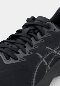 Black athletic shoe featuring a textured upper, lace closure, and reflective accents. The design includes a patterned side detailing.