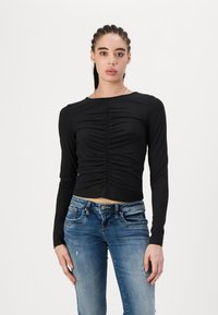 Svart, cropped langermet topp med rynkedetaljer foran, kombinert med lyseblå, slitte skinny jeans. Jevn stofftekstur.