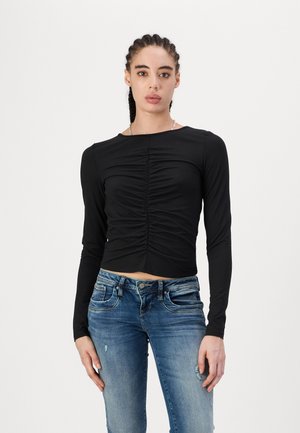 Black cropped long-sleeve top with gathering detail at the front, paired with light blue distressed skinny jeans. Smooth fabric texture.