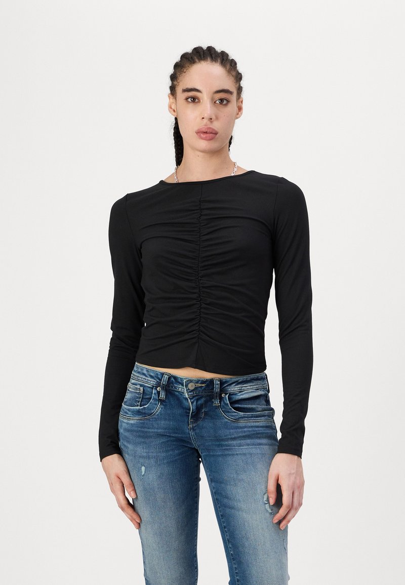 Svart, cropped langermet topp med rynkedetaljer foran, kombinert med lyseblå, slitte skinny jeans. Jevn stofftekstur.