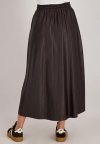 Midi-jurk van donkerbruin stof, met een elastische tailleband en een gladde, glanzende textuur. Gecombineerd met casual, gestructureerde sneakers.