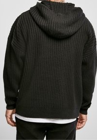 Black ribbed knit hoodie with a spacious hood, dropped shoulders, and a textured finish, featuring wide cuffs and a relaxed fit.