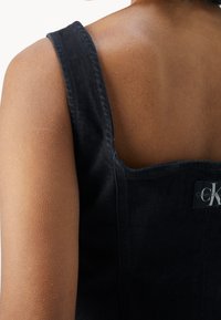 Czarny top d�żinsowy z kwadratowym dekoltem i szerokimi ramiączkami. Posiada metkę z logo Calvin Klein. Materiał ma teksturowany wygląd.