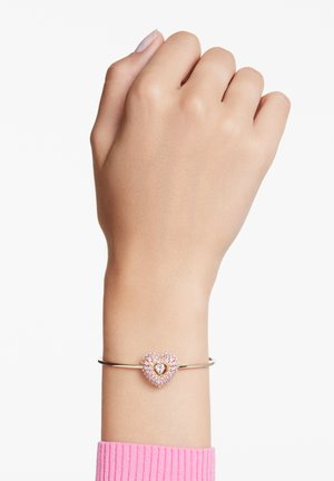 Roze gouden bangle armband met een hartvormige hanger bezet met roze rhinestones en een centraal gouden hartdetail.