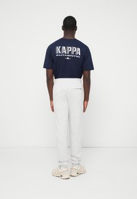 Granatowa koszulka Kappa z białym nadrukiem "AUTHENTIC", sparowana z jasnoszarymi spodniami dresowymi, posiadającymi elastyczne mankiety i pas.