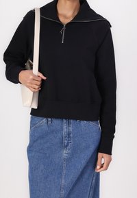 Black zip-up sweatshirt with a high collar and ribbed cuffs, paired with a light beige bag and blue denim skirt. Smooth texture.