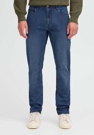 Blue denim jeans with a slim fit, five-pocket design, beaded texture, and silver button closure. Paired with white lace-up sneakers.