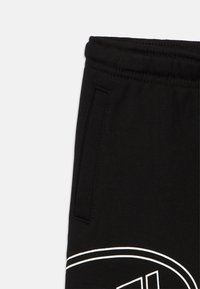 Μαύρο παντελόνι φόρμας από ύφασμα με ελαστική μέση, πλαϊνή τσέπη και μερικό λευκό κυκλικό λογότυπο κοντά στο τελείωμα.