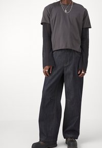 Dark gray cropped t-shirt over a long-sleeve top, paired with wide-leg dark blue denim pants. Notable silver hardware accents.