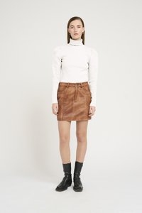 Jupe en cuir marron avec coutures visibles et passants de ceinture, associée à un col roulé à manches longues en maille blanche et des bottines noires.