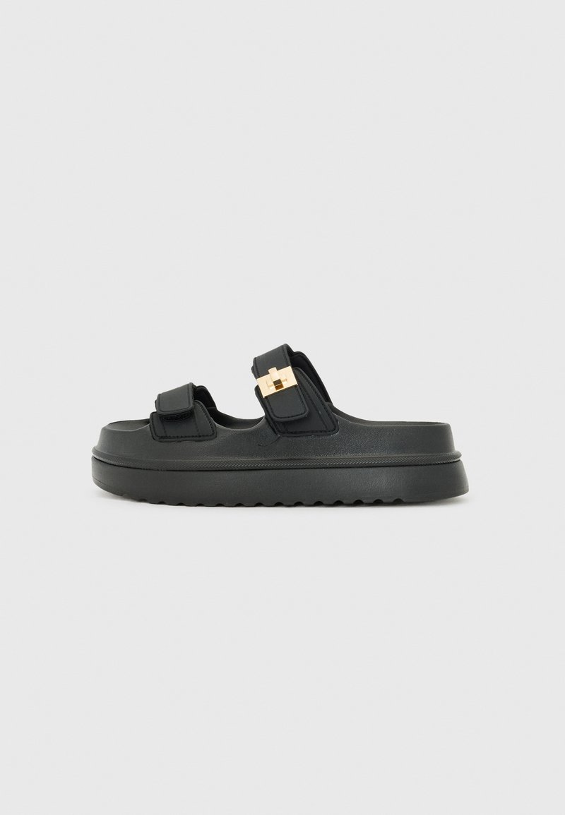 Black sandals with two adjustable straps, gold hardware accents, thick platform sole, and textured footbed. Smooth material finish.