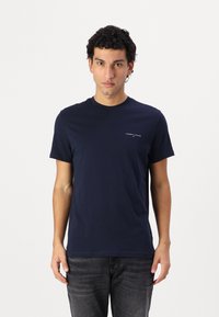 Navyblaue Baumwoll-T-Shirt mit Rundhalsausschnitt, kurzen Ärmeln und einem kleinen weißen Logo auf der linken Brustseite. Minimalistisches Design und glatte Textur.