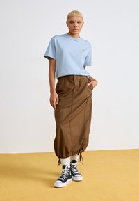 Lichtblauw katoenen t-shirt, losse pasvorm, bruine cargorok met drawstring zoom, en zwarte high-top sneakers met witte veters. Zachte textuur.