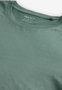 Camiseta de algodón verde con cuello redondo, corte regular y textura suave, con una etiqueta que indica la talla M y su origen.