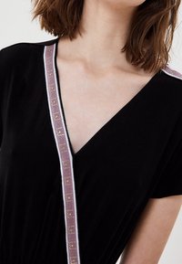 Schwarzes Kleid mit V-Ausschnitt. Dekorative rosa und weiße Streifen mit Metallnieten entlang des Ausschnitts verziert.