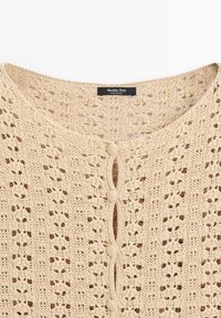 Beige gebreid vest met bloemenkantpatroon, ronde halslijn, met stof beklede knopen en Massimo Dutti-label.