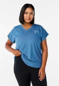 Korte mouwen, V-hals sporttop van blauwe stof met een soepele textuur. Voorzien van een subtiele logo-detail. Gecombineerd met zwarte leggings.