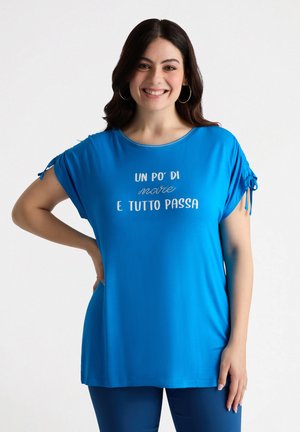 Top azul de manga corta hecho de tela suave, con cuello redondo y acentos fruncidos en las mangas. Texto blanco impreso en la parte delantera.
