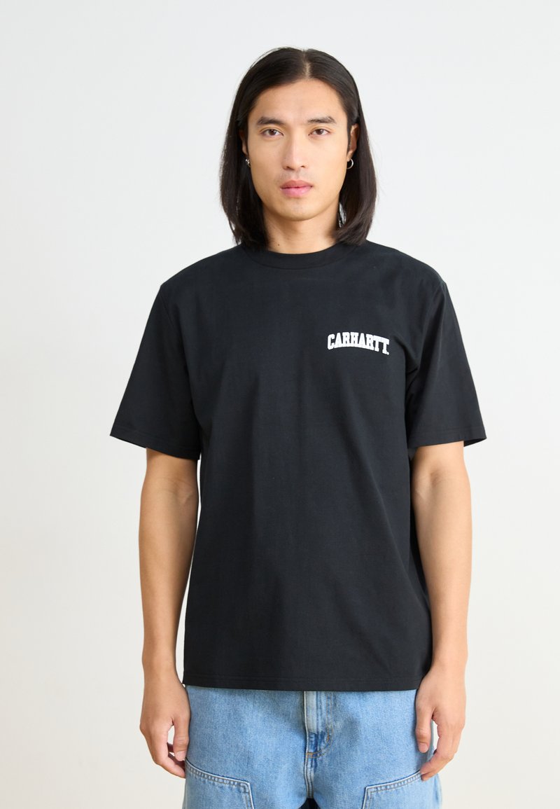 Czarny bawełniany t-shirt z krótkim rękawem, z białym logo "Carhartt" na górnej lewej części klatki piersiowej, w zestawie z niebieskimi dżinsami.