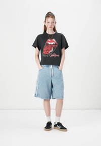 Black cropped t-shirt with red graphic lips and teeth design, paired with light blue denim shorts featuring side stripes and elastic waistband.