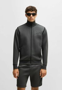 Mörkgrå idrottsjacka med hög krage, dragkedjestängning och framfickor. Matchande shorts i samma material, båda i en slät tyg.
