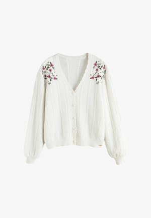 White knitted cardigan with cable patterns, button closure, and pink floral embroidery on shoulder areas and long puffed sleeves.