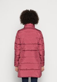 Abrigo acolchado en rosa intenso, con cuello alto y diseño acolchado. La tela tiene un acabado suave con costuras visibles.