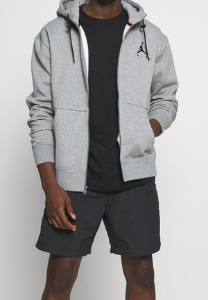Grijze zip-up hoodie met een zwart logo op de borst, voorzien van een trekkoordcapuchon en geribde manchetten, gecombineerd met een zwarte short.
