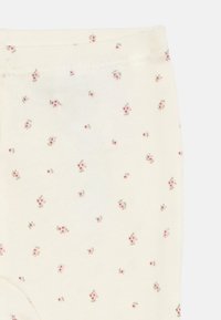 Leggings de cor creme com uma textura suave, apresentando um padrão floral disperso em rosa e verde. Cintura elástica no topo.