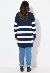 Námořnický a bílý pruhovaný dlouhý svetr s rib strukturou, s dlouhými rukávy. V kombinaci s ohrnutými světle modrými džíny a černými botami.