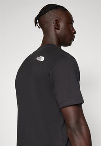 Czarny bawełniany T-shirt z krótkim rękawem, z białym logo na górnej części pleców. Prosty design, okrągły dekolt, regularny krój.
