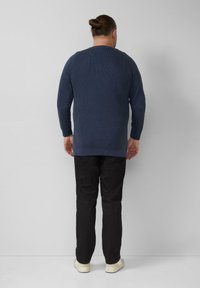 Blauer, gerippter Strickpullover mit langen Ärmeln, rundem Ausschnitt und lockerer Passform, kombiniert mit schwarzer Hose und weißen Turnschuhen.