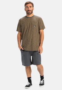 Gestreepte T-shirt met korte mouwen in bruin en beige, featuring een ronde hals en een logo op de linkerborst. Gecombineerd met grijze cargoshorts en sneakers.