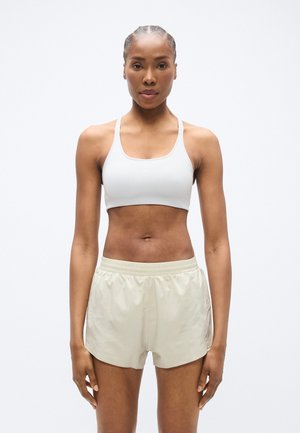 Sutien sport în gri deschis, cu bretele subțiri, asortat cu pantaloni scurți bej care au panouri laterale din plasă și talie elastică.