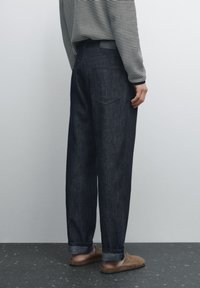 Mörkblå denimjeans med lös passform, med uppvikta ben, två bakfickor och ett enkelt midjeband. Matchas med en randig långärmad skjorta.