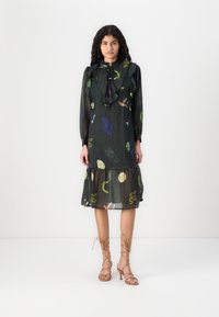 Robe noire à motifs abstraits colorés, col volanté, manches longues et ourlet en couches. Associée à des sandales à talons hauts marron clair avec des lanières.