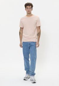 Light pink striped t-shirt with short sleeves, paired with blue jeans and gray sneakers. Includes tattoos on visible arms.