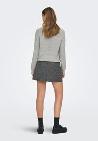 Pull en tricot gris, jupe courte en tweed noir, chaussures noires épaisses et chaussettes foncées. Texture lisse, design simple, sans motifs prononcés.