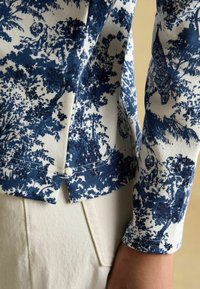 Tumesinine lillemustriga valge kangas, millel on tekstureeritud, ribalik disain. Kleidil on jagatud hem ja sobitatud vars.