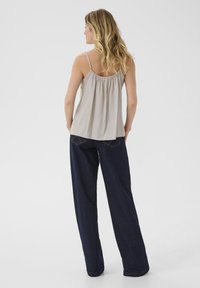 Svetlo bež brezrokavni top s nabrano hrbtno zasnovo, v kombinaciji s temno modrimi širokimi hlačami z zadnjimi žepi in zlatimi nitmi.