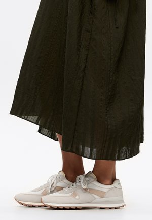 Lichtbeige sportieve schoenen met een gestructureerde suede en mesh bovenkant, bijpassende veters en een gumrubberen zool, gedragen onder een lange, donkergroene rok.