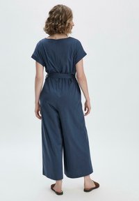 Combinaison bleu marine à manches courtes, taille ceinturée et coupe large. Tissu doux avec un discret détail de bouton au dos.