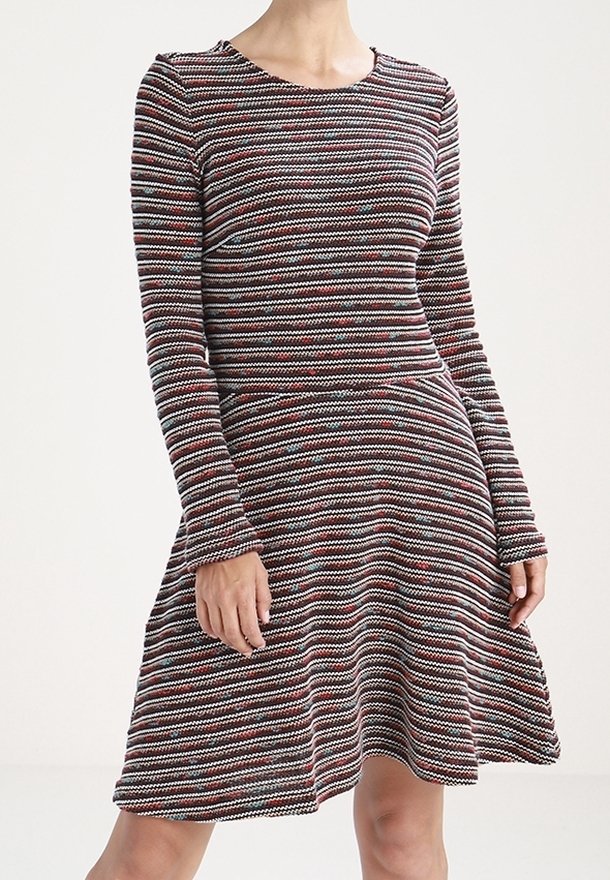 Femme portant une robe à manches longues, longueur genou, avec des rayures horizontales multicolores et une taille cintrée.
