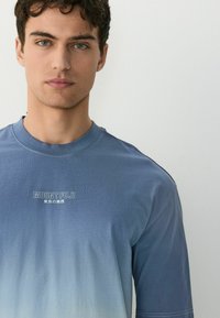 Blå gradient T-shirt med korte ærmer. Har teksten "MOUNT FUJI" i hvid. Blødt stof med glat tekstur. Enkel, afslappet design.