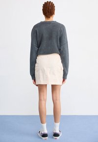 Grå oversized genser, lys beige skjørt med cargo-lommer, parret med hvite sokker og svarte joggesko. Fléttet hår stylet bak.
